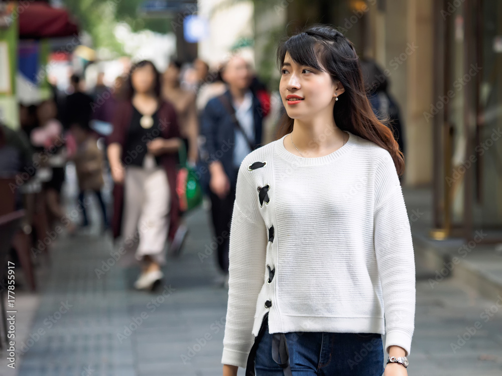 Autumn portrait of happy Chinese girl on a walk in crowded street in Shanghai, China.