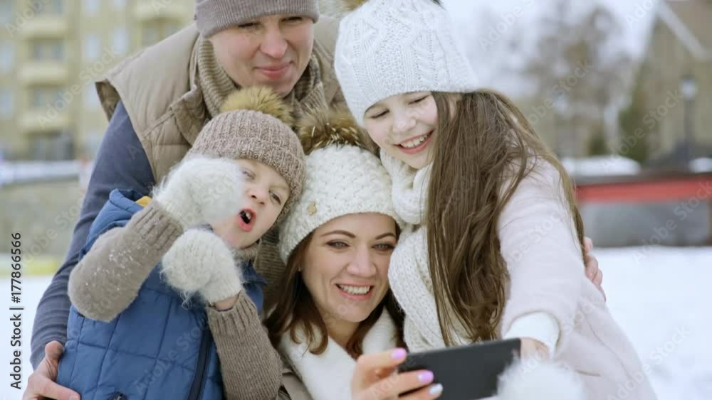 Medium shot of happy mother, father and children taking selfie outdoor in winter Medium shot of happy mother, father and children taking selfie outdoor in winter