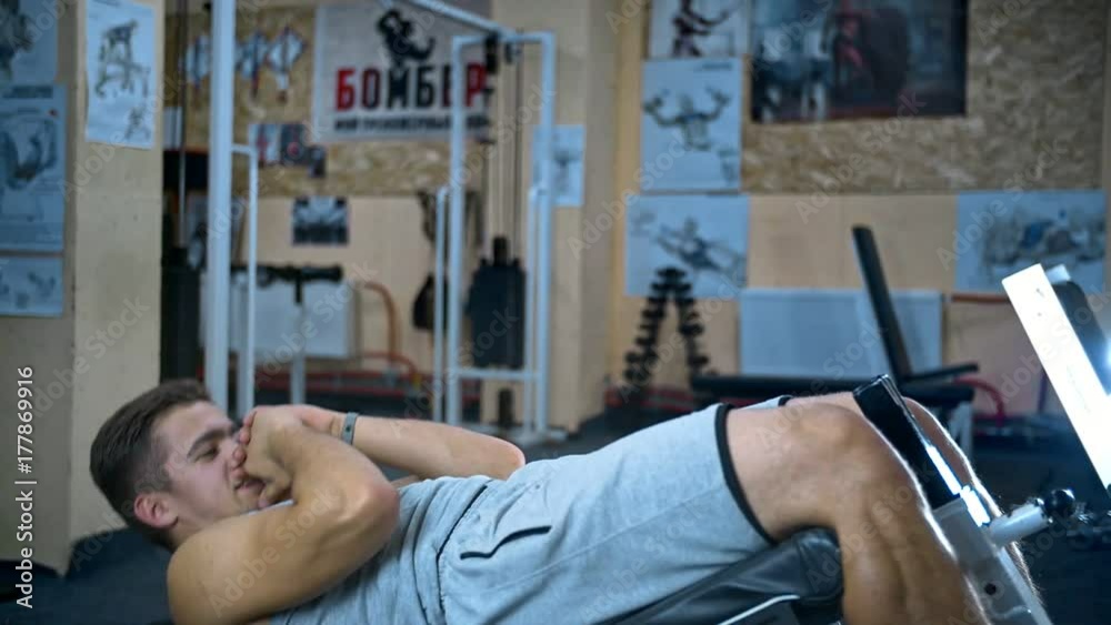 Young man doing sit-ups on abdominal bench and getting tired abdominal exercises Young man doing sit-ups on abdominal bench and getting tired abdominal exercises