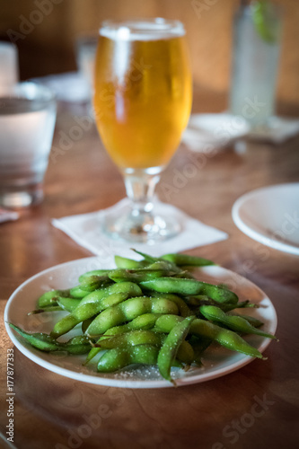A plate of fresh green edamame with a glass of beer in the background