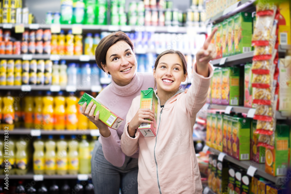 attentive woman with daughter choosing refreshing beverages in supermarket