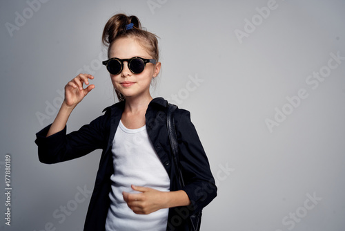 a little girl in black glasses and black clothes on a gray background. empty space for copying
