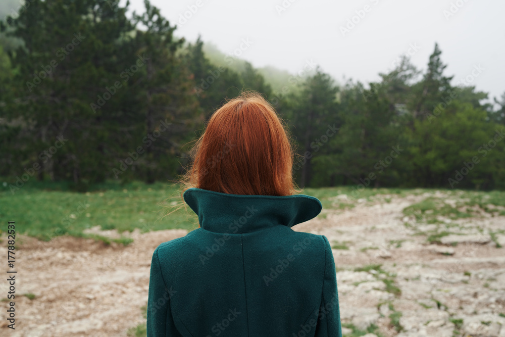 a woman in a green coat strolling through the woods
