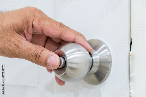 Hand pressing door knob mounted on a white wooden door.