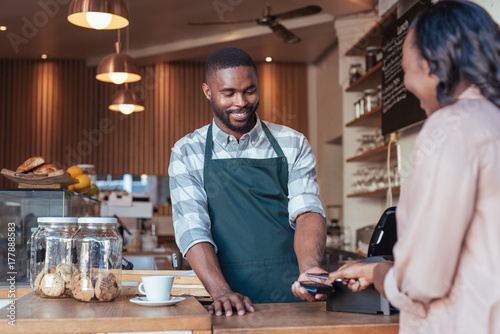 Quadro su tela Smiling barista using nfc technology for a customer's payment