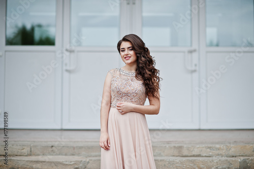 Portrait of an attractive girl standing and posing on the stairs in amazing gowns after high school graduation.