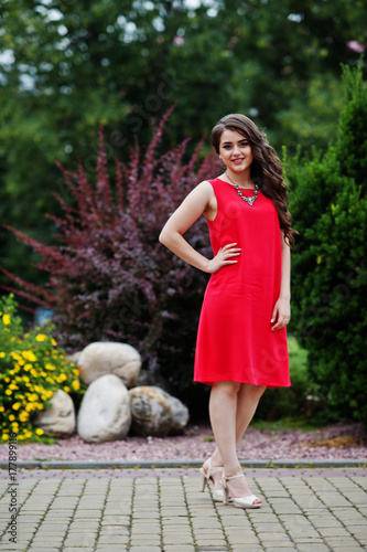 Portrait of an attractve young girl in red dress posing on the pavement in the park on a prom day. photo