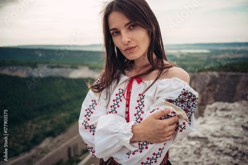 Atractive woman in traditional romanian costume on mountain green blurred background. Outdoor photo. Traditions and cultural diversity