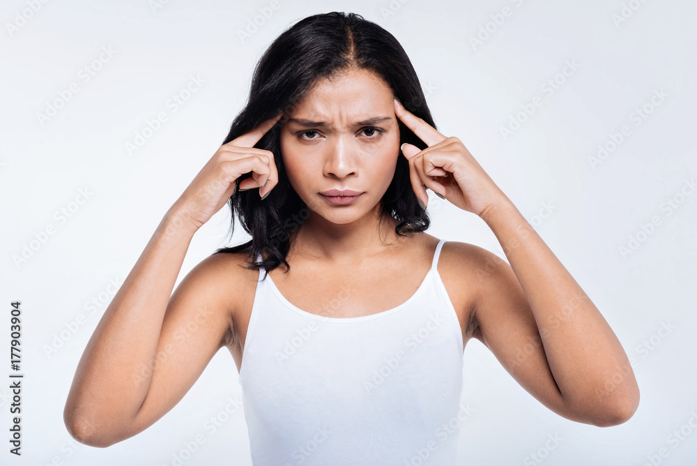 Dark-haired young woman pressing fingers to temples Dark-haired young woman pressing fingers to temples