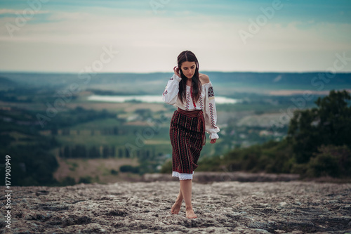 Atractive woman in traditional romanian costume on mountain green blurred background. Outdoor photo. Traditions and cultural diversity