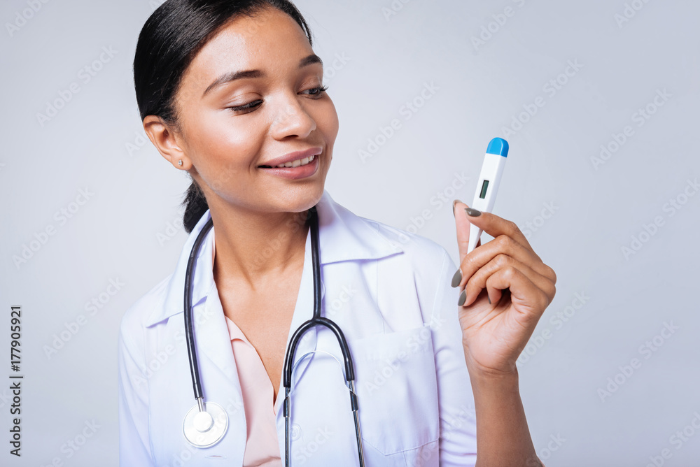 Cheerful female doctor looking at thermometer in her hand Cheerful female doctor looking at thermometer in her hand