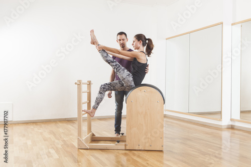 Pilates lesson on barrel, personal trainer coaching young beautiful woman