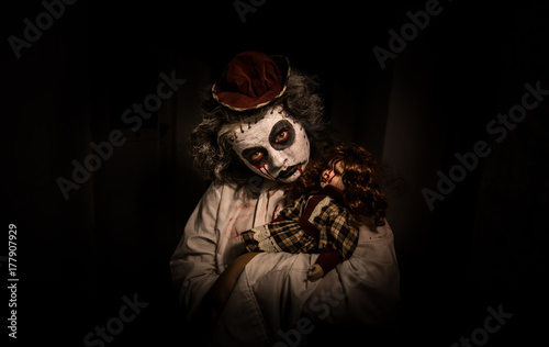Horror movie scene.Creepy girl with bloody doll in a scary dark room