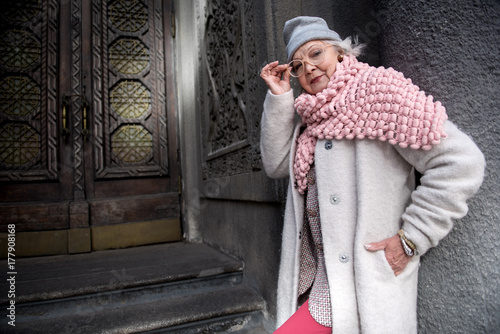 Confident fashionable senior woman posing near ancient door