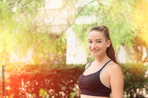 Beautiful smiling young woman with ponytail, breathing fresh air in the park. Woman enjoying yoga, relaxing, got freedom. Copy space background. Side view portrait. Sunlight. Gym, lifestyle concept.