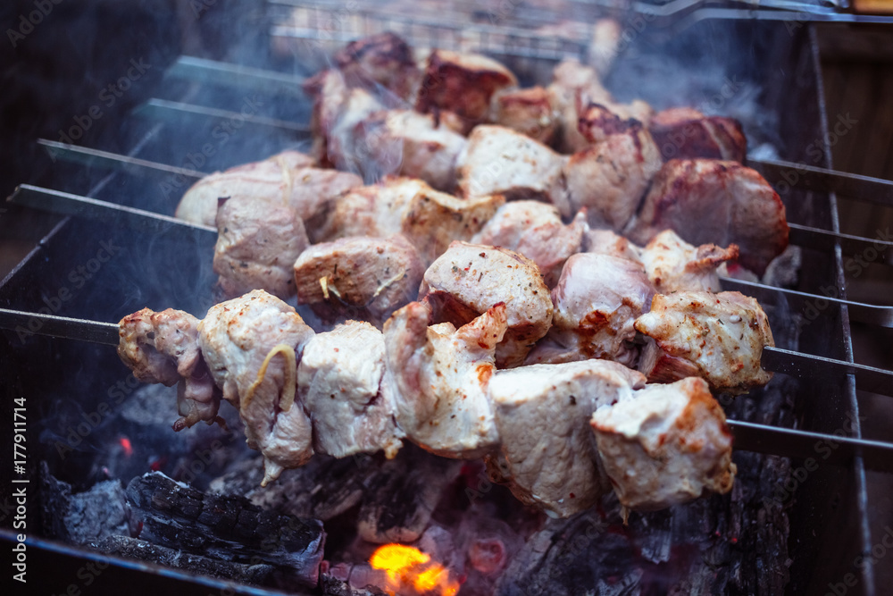 Grilled kebab cooking on metal skewers (grill). Roasted meat cooked at barbecue with smoke. Close up BBQ fresh pork meat chop slices. Traditional eastern dish, shish kebab. Grilled kebab cooking on metal skewers (grill). Roasted meat cooked at barbecue with smoke. Close up BBQ fresh pork meat chop slices. Traditional eastern dish, shish kebab.