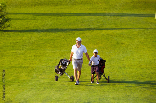 man with his son golfers walking on perfect golf course at summer evening
