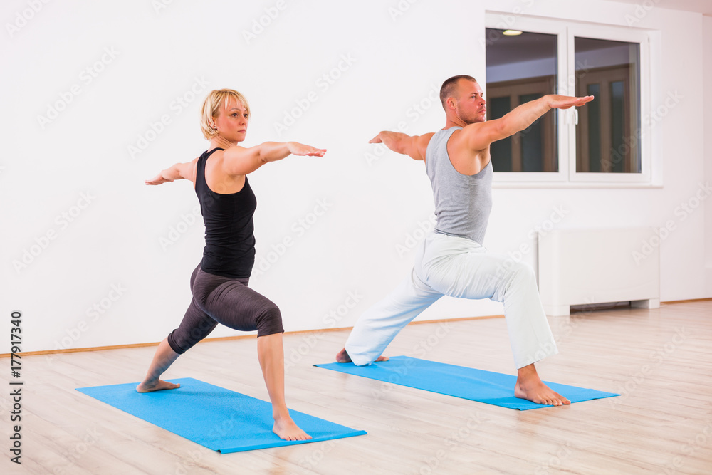 Adult man and woman practicing yoga, Virabhadrasana / Warrior 2 pose