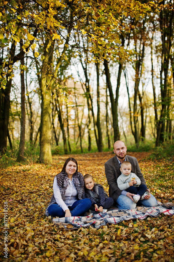 Happy caucasian family of mom dad and little girl with boy sitting on plaid at majestic autumn fall forest. Happy caucasian family of mom dad and little girl with boy sitting on plaid at majestic autumn fall forest.