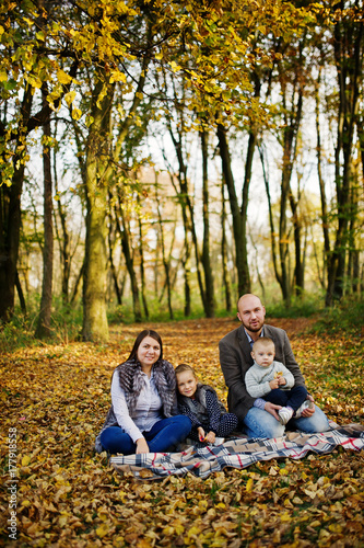 Happy caucasian family of mom dad and little girl with boy sitting on plaid at majestic autumn fall forest.