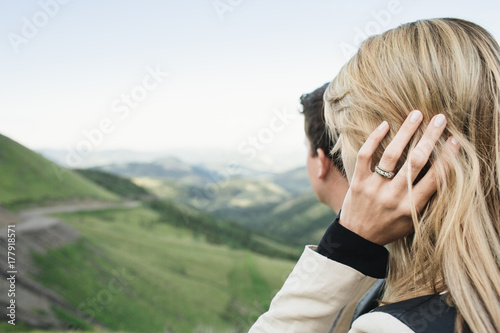 A blonde woman and her fianc?? looking out into a valley with a diamond ring on her finger