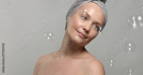 30's woman wears a towel after bath surrounded by soap bubbles looking at camera Slow motion footage