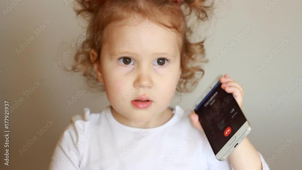 Happy little girl smilling, calls by mobile phone and talks. A funny child speaks on a smartphone, a close-up portrait. Happy little girl smilling, calls by mobile phone and talks. A funny child speaks on a smartphone, a close-up portrait.