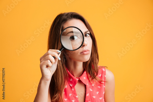Close-up portrait of young serious woman looking through a magnifying glass photo