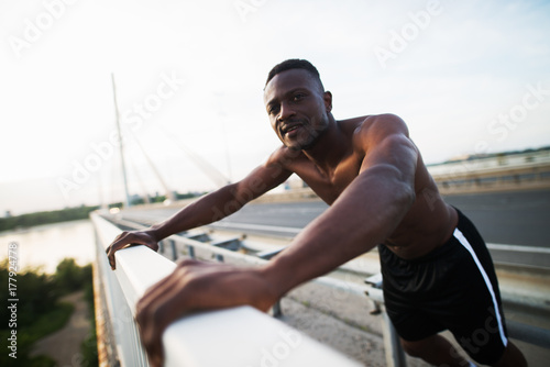 Handsome afro-american runner resting on the bridge between fences in the morning. © dusanpetkovic1
