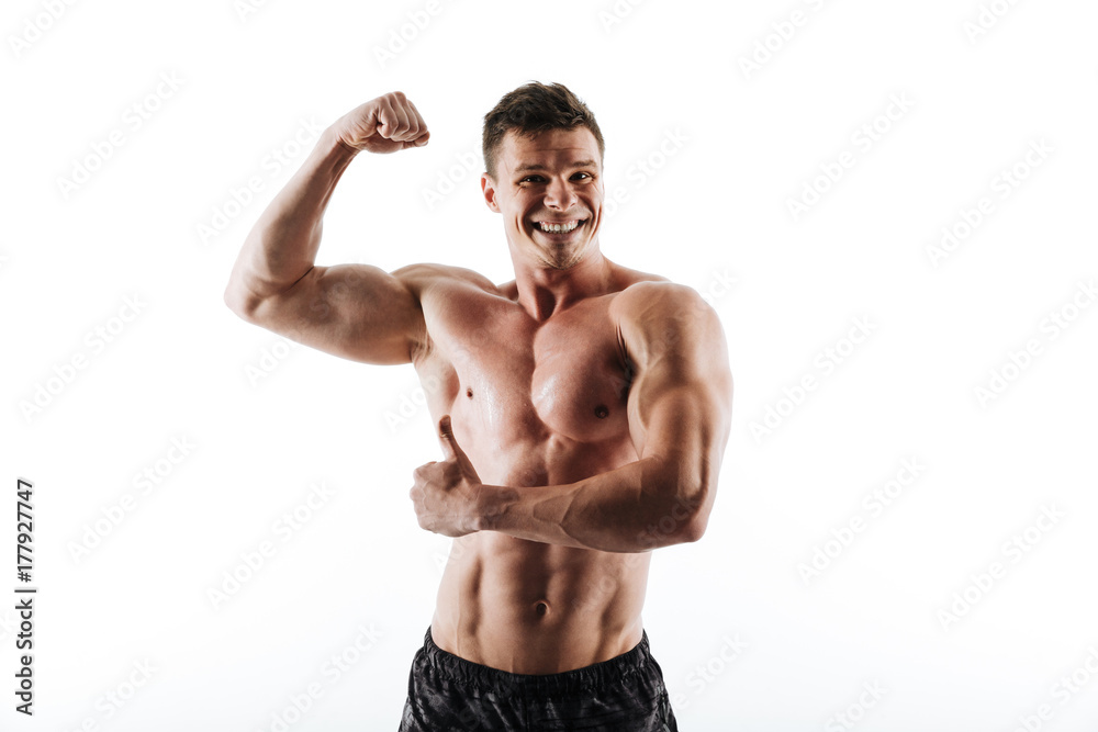 Portrait of young laughing muscular man showing his biceps and thumb up gesture, looking at camera