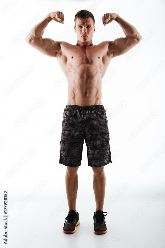 Full-length photo of strong and powerful sports man in black shorts showing his biceps, looking at camera Full-length photo of strong and powerful sports man in black shorts showing his biceps, looking at camera