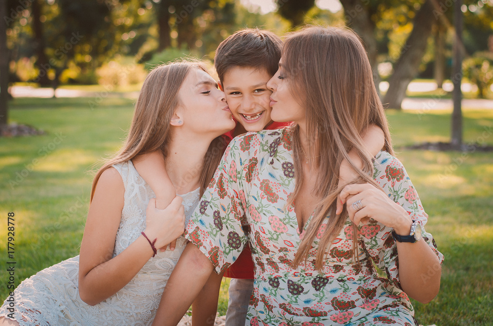 Happy mother, son and daughter in the park. Mom and sister kiss their son. Happy family concept. Happy mother, son and daughter in the park. Mom and sister kiss their son. Happy family concept.