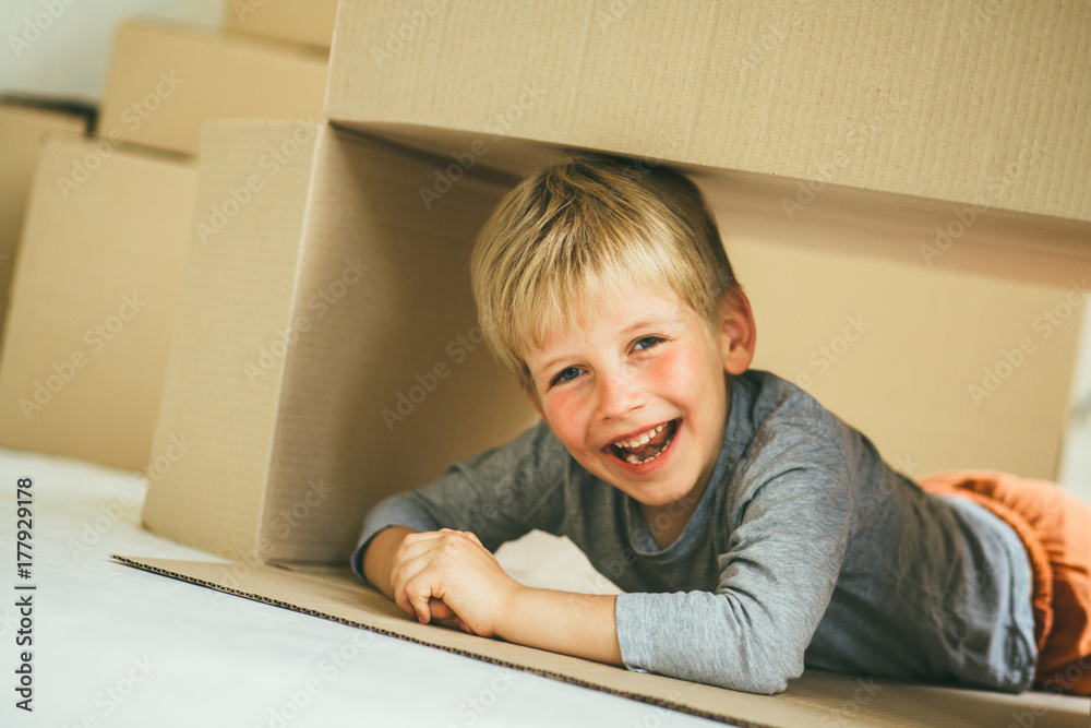Rose cheeks preschooler boy sitting inside box in new house. Child lying on the floor, laughing and looking froom cardboard box. Toned.