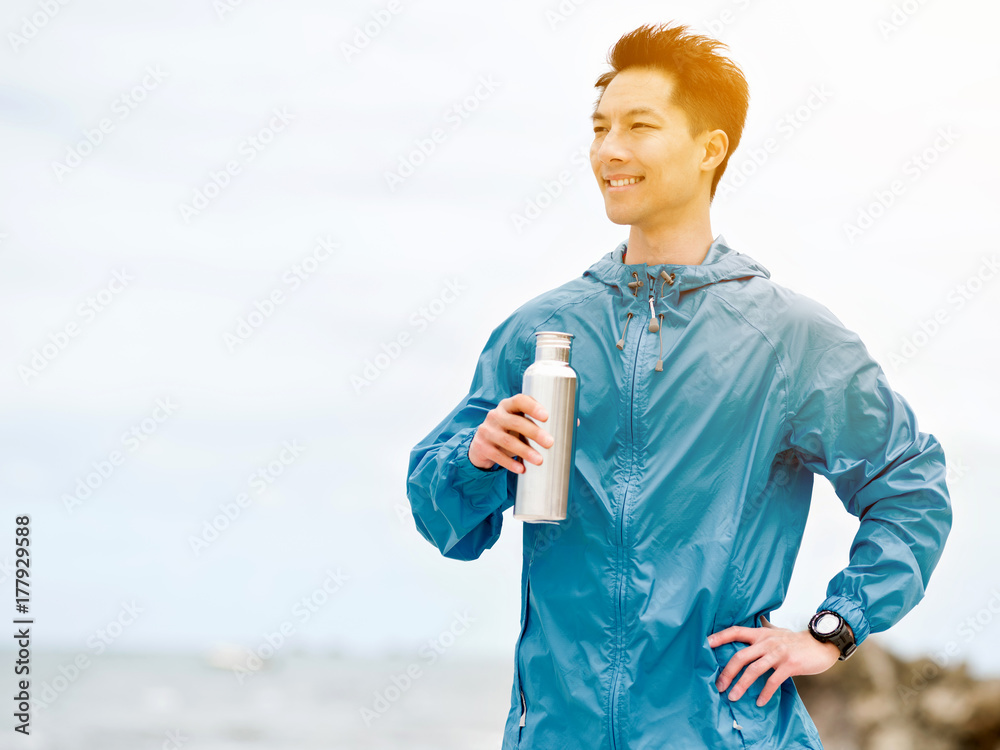 Young man in sport clothes drinking water after workout on the beach Young man in sport clothes drinking water after workout on the beach