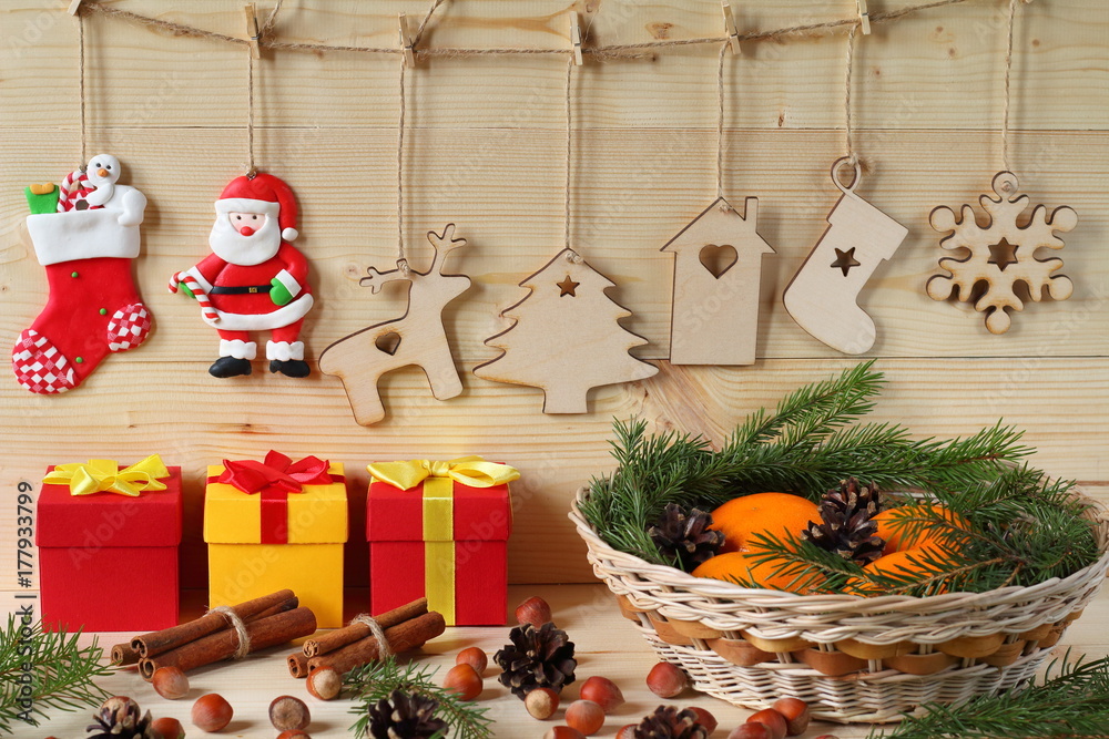 Fototapeta premium Christmas and New Year composition. Composition of Christmas and New Year decorations from plywood, a wicker basket with tangerines, color gift boxes, nuts and fir branches on a wooden background.