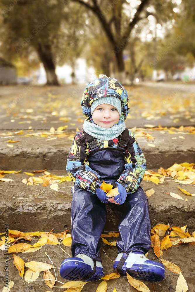 A child, a boy is sitting on the steps, a walk in the fall in the rain A child, a boy is sitting on the steps, a walk in the fall in the rain