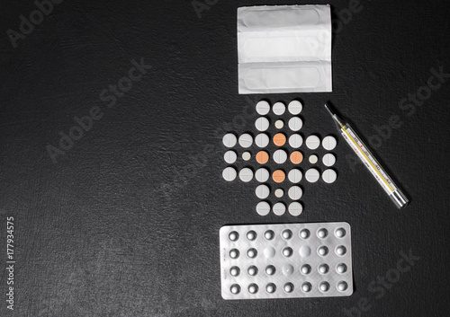 Tablets lined in the form of a cross on a dark background with packets of pills and a thermometer, top view © Maksim