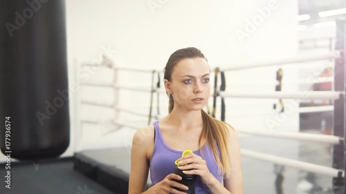 Female caucasian boxer drinking water from the black sportsbottle near the boxing ring photo
