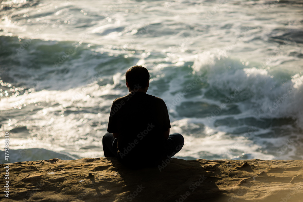 Silhouette of man sitting on sunset cliffs in San Diego california watching ocean