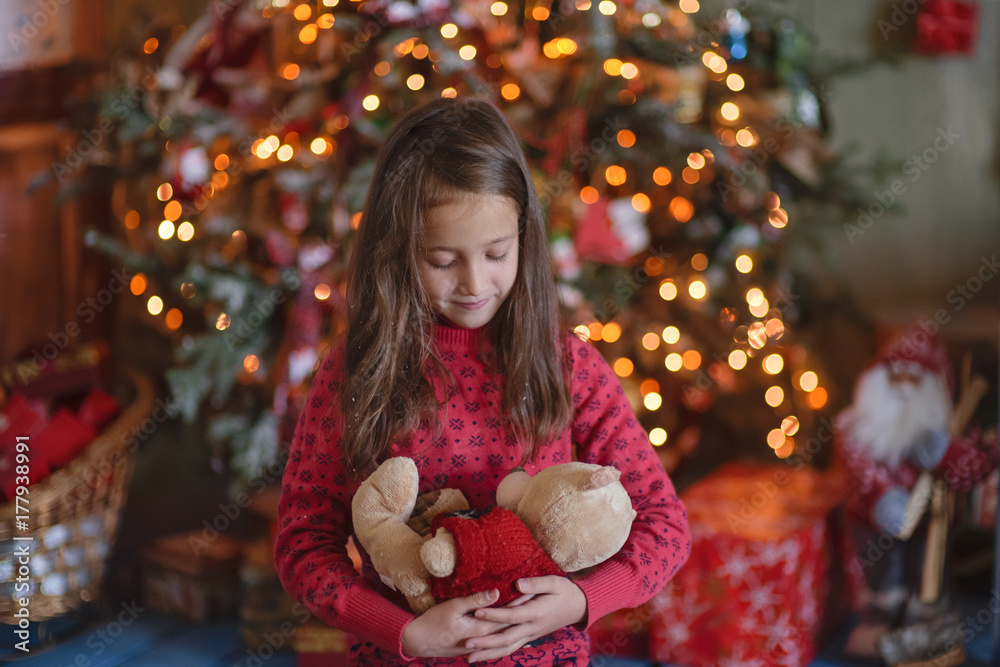 The girl against the background of a Christmas tree plays with a toy bear The girl against the background of a Christmas tree plays with a toy bear