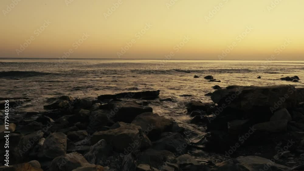 Small waves roll on a stony shore at sunset with a clear horizon Small waves roll on a stony shore at sunset with a clear horizon