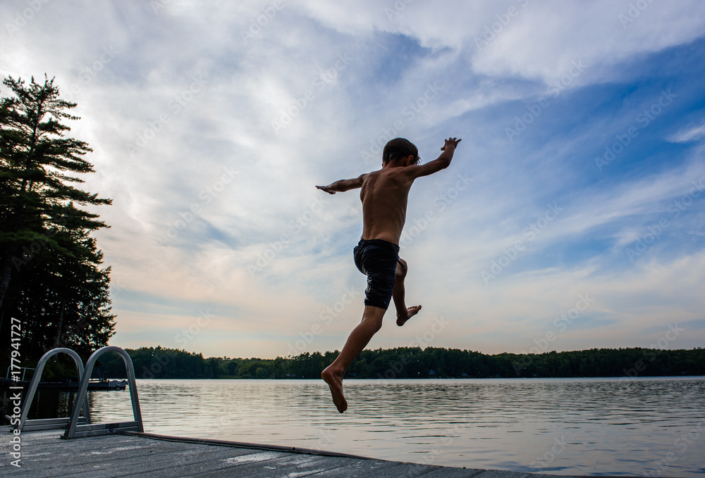 Child jumps off a dock into a lake on a summer evening Child jumps off a dock into a lake on a summer evening