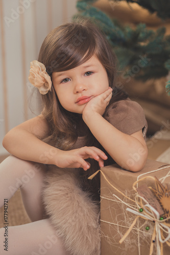 Young brunette dolly lady girl stylish dressed cozy warm winter gray jacket with fur posing sitting standing in studio close to Christmas New Year tree and presents.