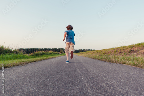 Boy running away on a long road in the fields