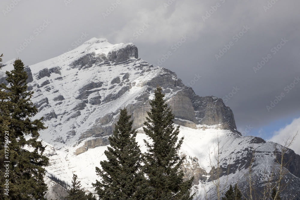 A close-up view of a snow covered mountain with grey clouds hovering above in Banff National Park.