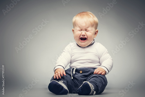 Crying baby sitting on the ground. Fotobehang