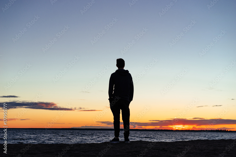 A young guy on the beach looking at the sunset