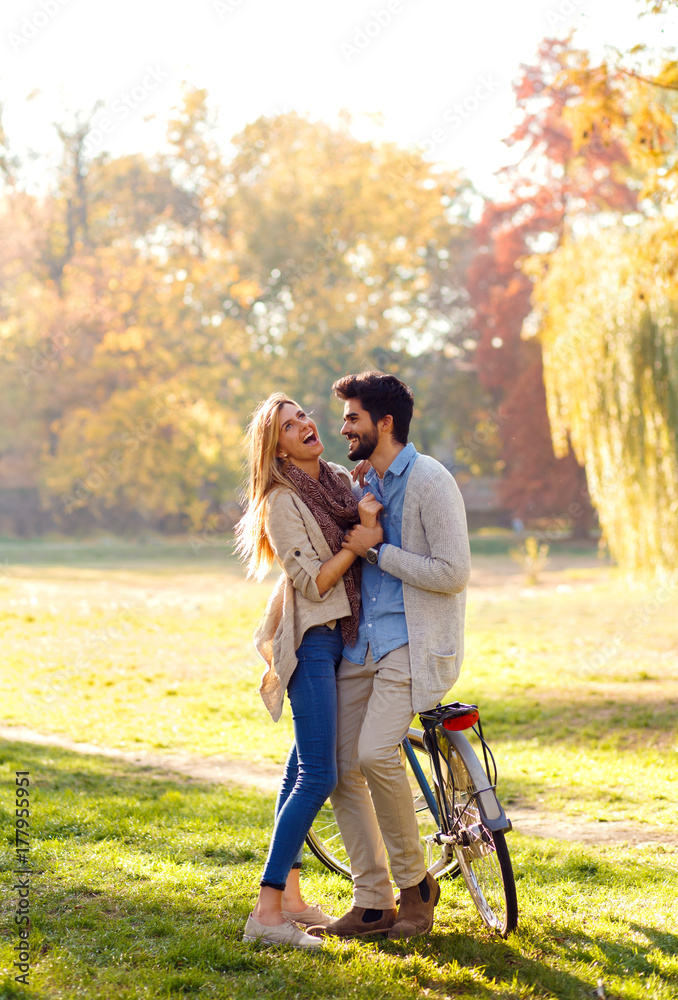 Young couple with bicycle standing in park on sunny autumn day.