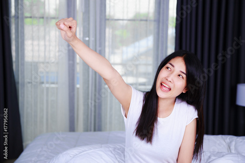 happy woman with hand raised on bed in bedroom