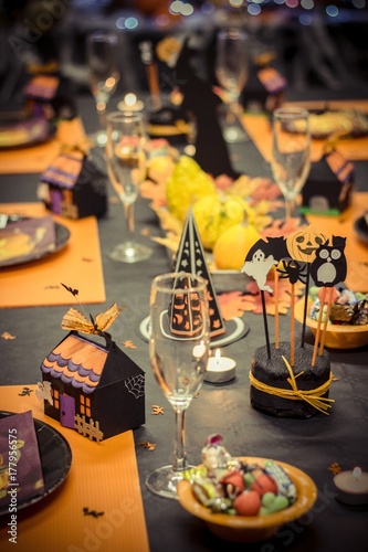 Table de réception avec une nappe noire et des décorations pour les fête d'halloween,une petite maison en carton , des verres et des assiettes en cartons